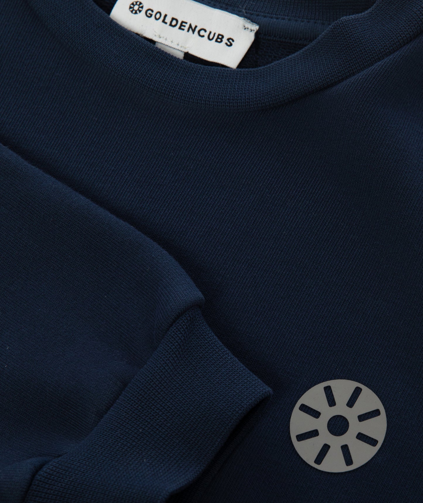 Close-up of Goldencubs gray circular logo printed on smooth navy cotton sweatshirt fabric.