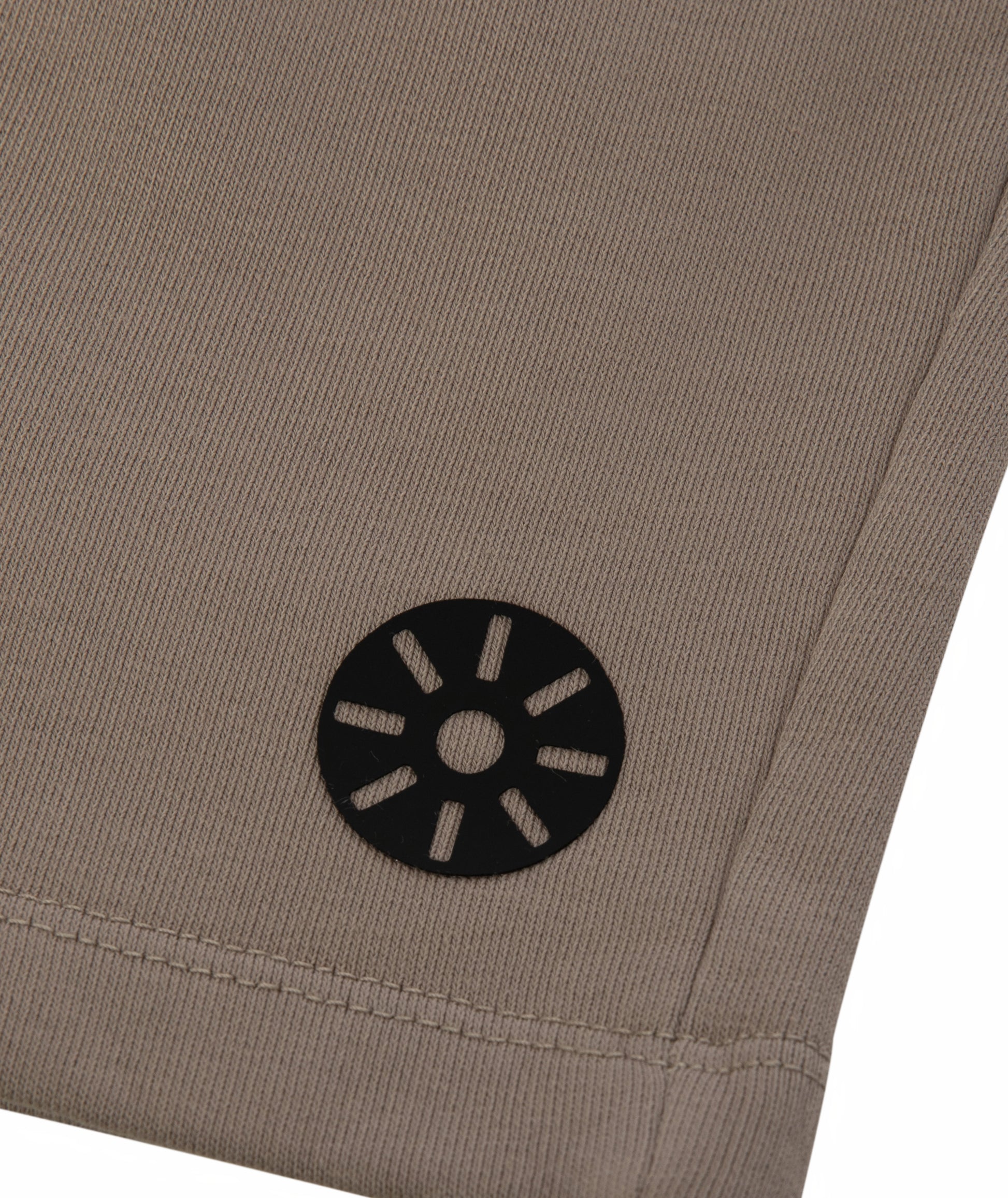 Close-up of Goldencubs black circular logo printed on soft taupe cotton fabric near hemline.