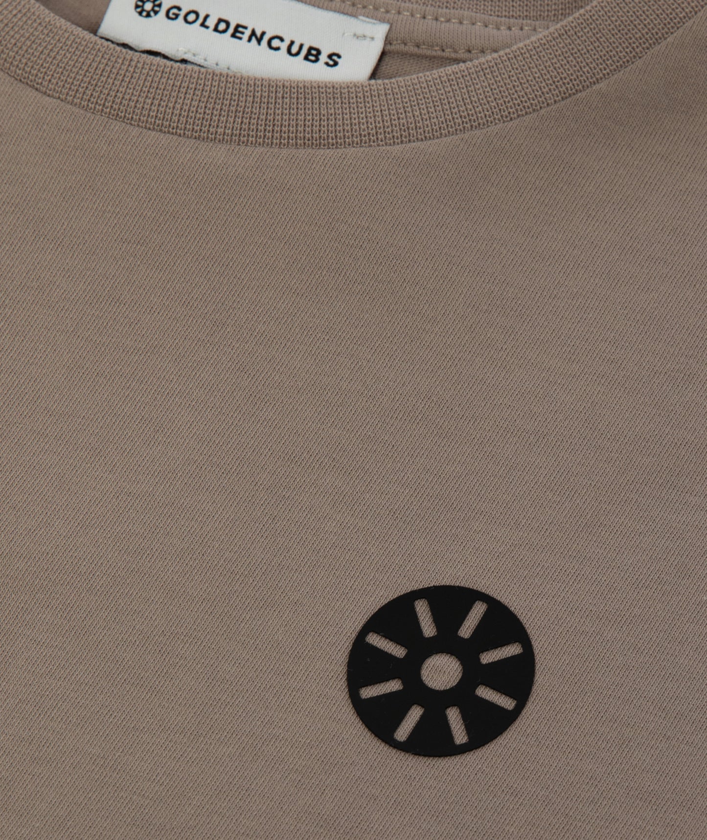 Close-up of Goldencubs signature black circular logo printed on taupe ribbed cotton fabric.