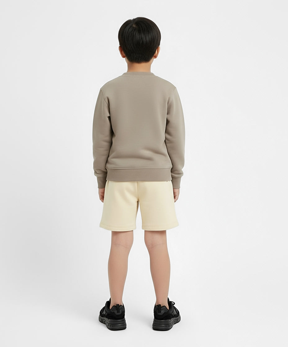 Back view of boy wearing Goldencubs cream cotton boys shorts and taupe sweatshirt — simple and modern kids athleisure outfit.