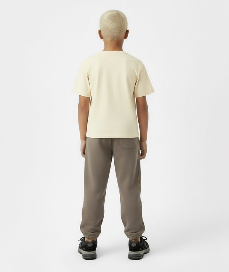 Back view of boy wearing Goldencubs cream cotton T-shirt with taupe sweatpants — soft, versatile, and stylish everyday kidswear.