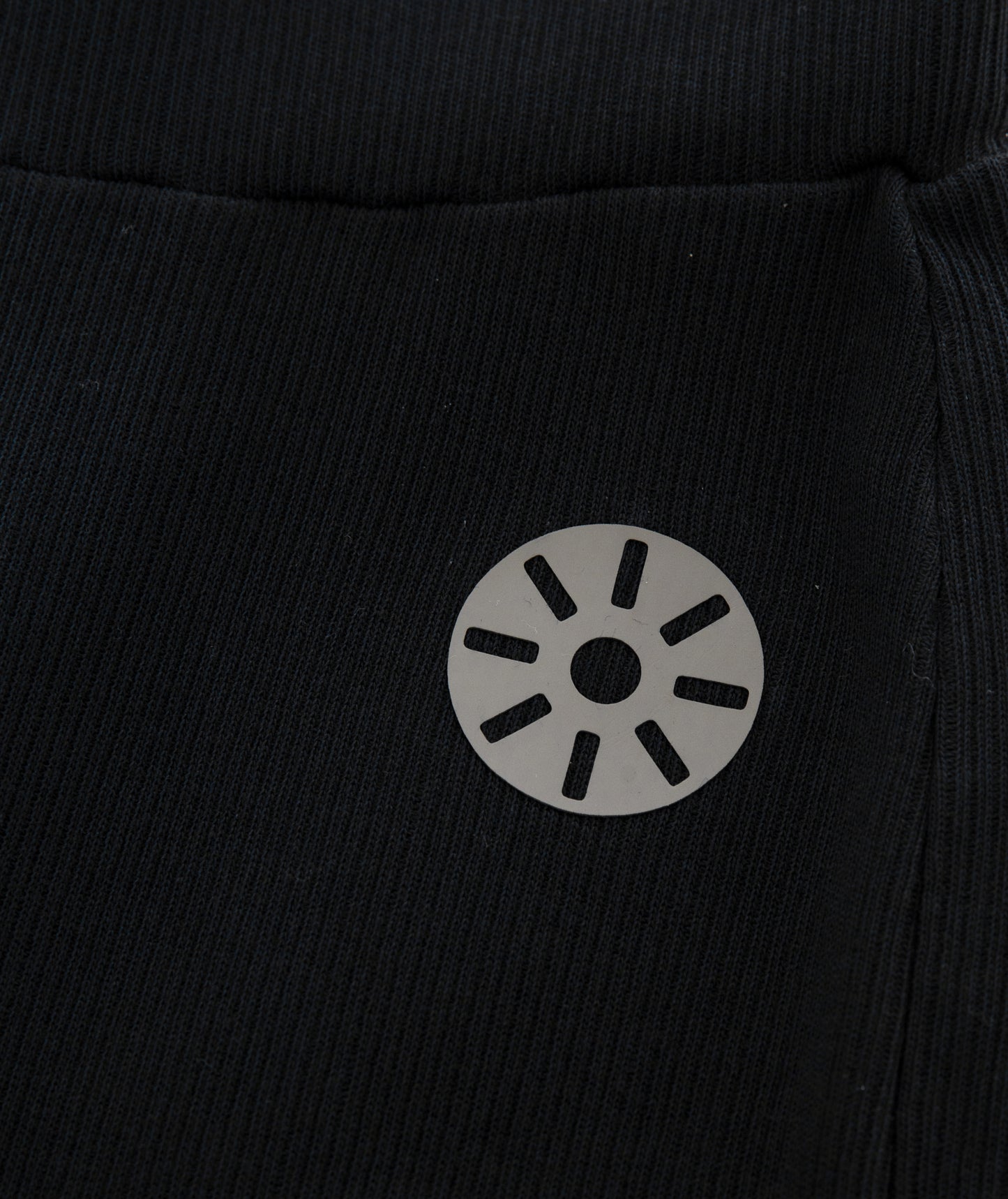 Close-up of Goldencubs reflective logo printed on ribbed black cotton flared pants fabric.
