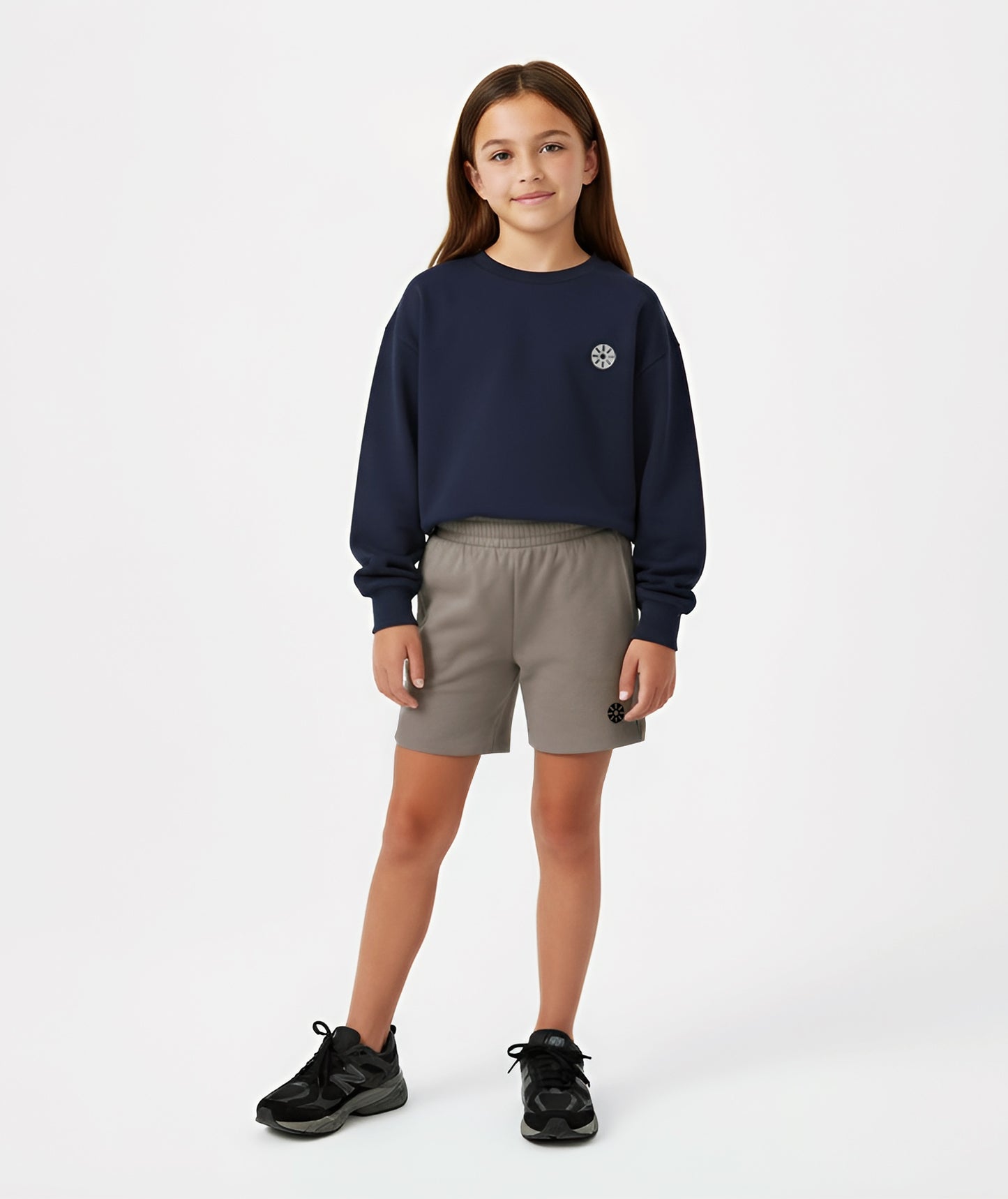 Girl wearing Goldencubs navy cotton sweatshirt with gray circular logo, styled with taupe shorts and black sneakers.