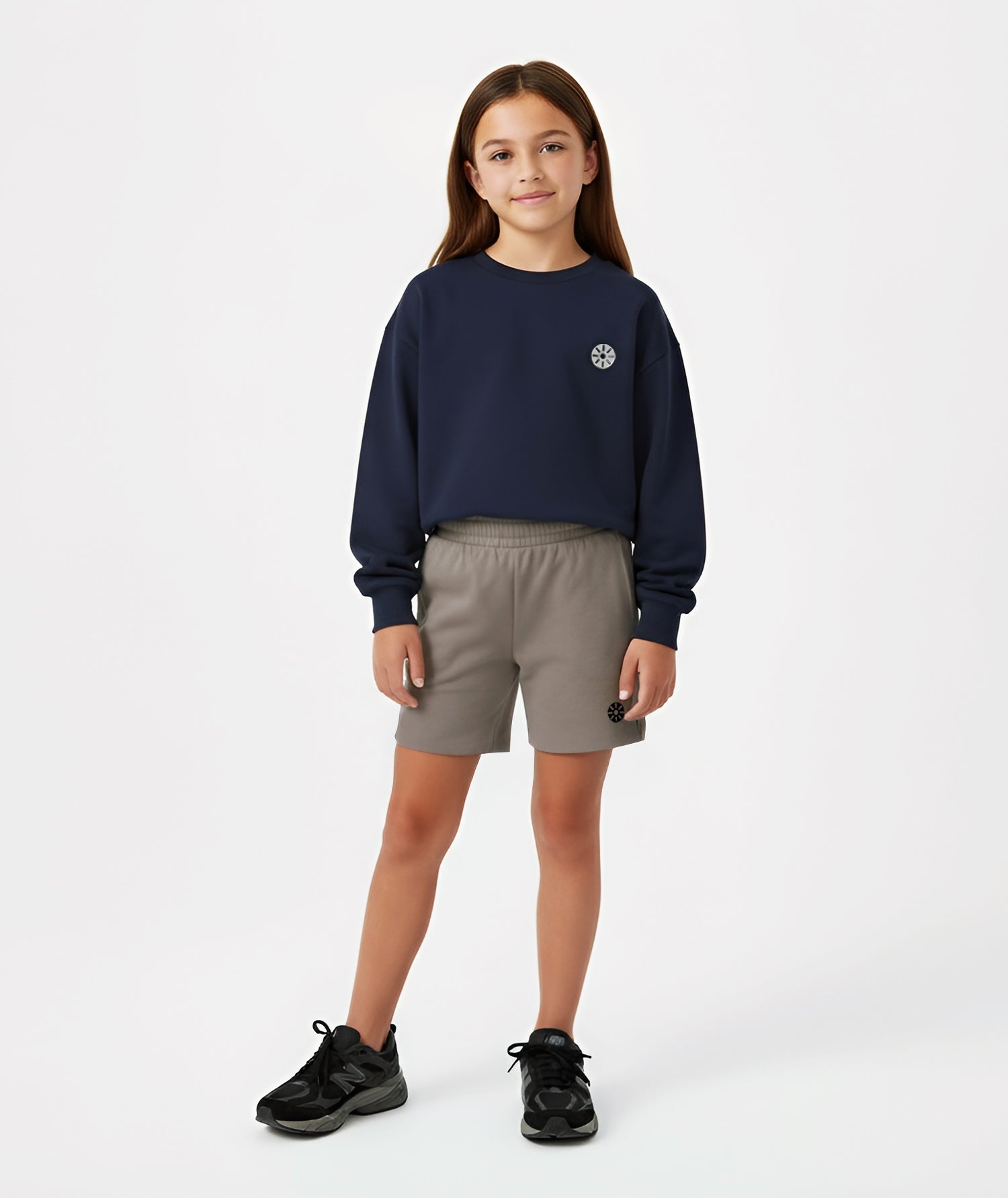 Girl wearing Goldencubs navy cotton sweatshirt with gray circular logo, styled with taupe shorts and black sneakers.