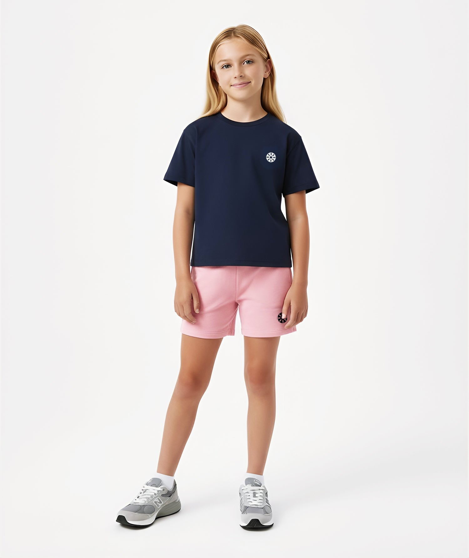 Girl wearing Goldencubs navy cotton T-shirt with gray circular logo, paired with pink shorts and gray sneakers.