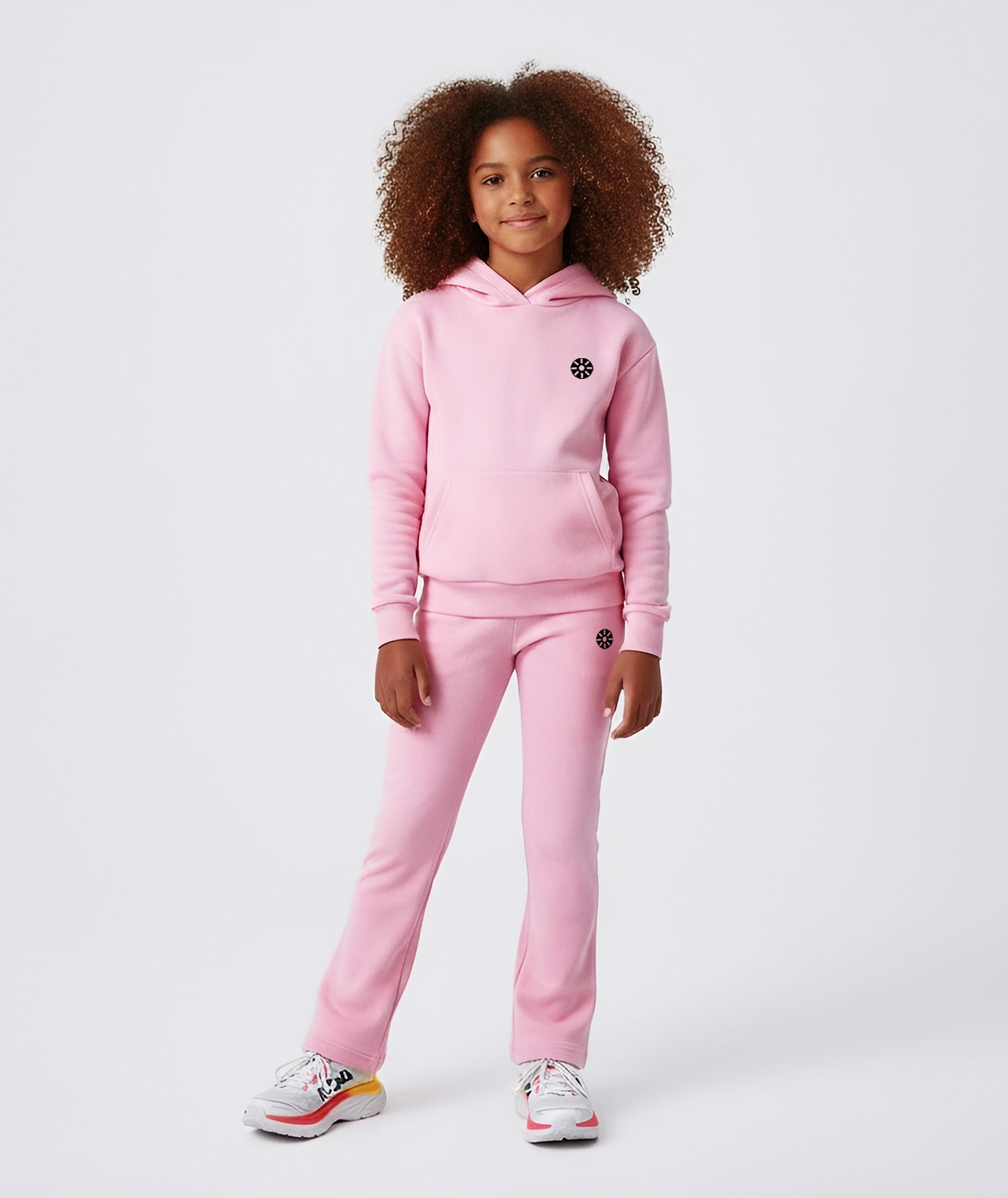 Girl wearing Goldencubs pink cotton flared pants with black circular logo, styled with matching hoodie and sneakers.