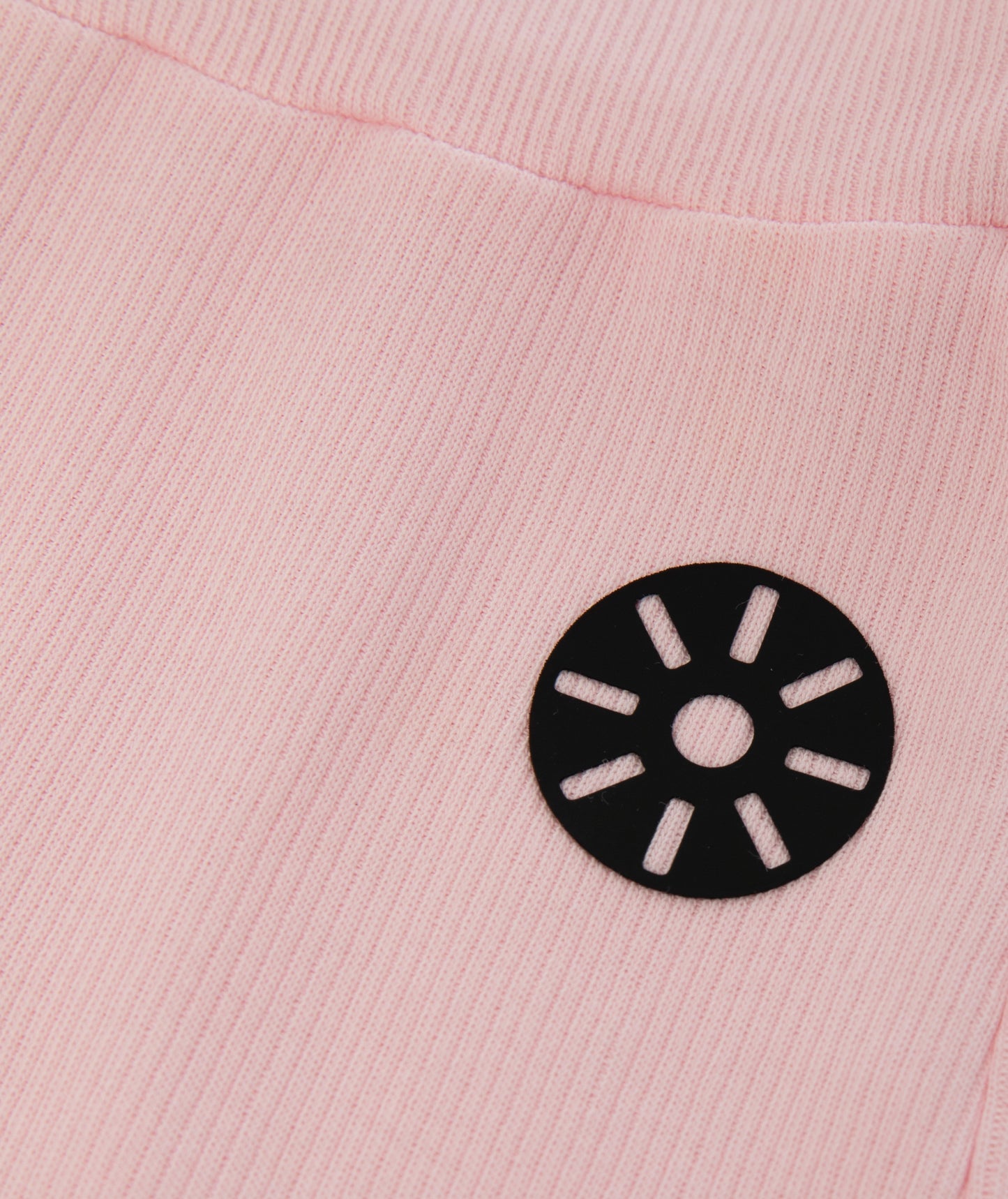 Close-up of Goldencubs black circular logo printed on soft pink ribbed cotton fabric of the flared pants.