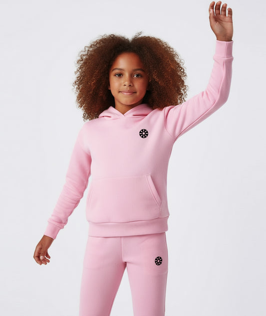 Girl smiling and raising hand while wearing Goldencubs pink cotton hoodie and flared pants, showing cozy and playful style.