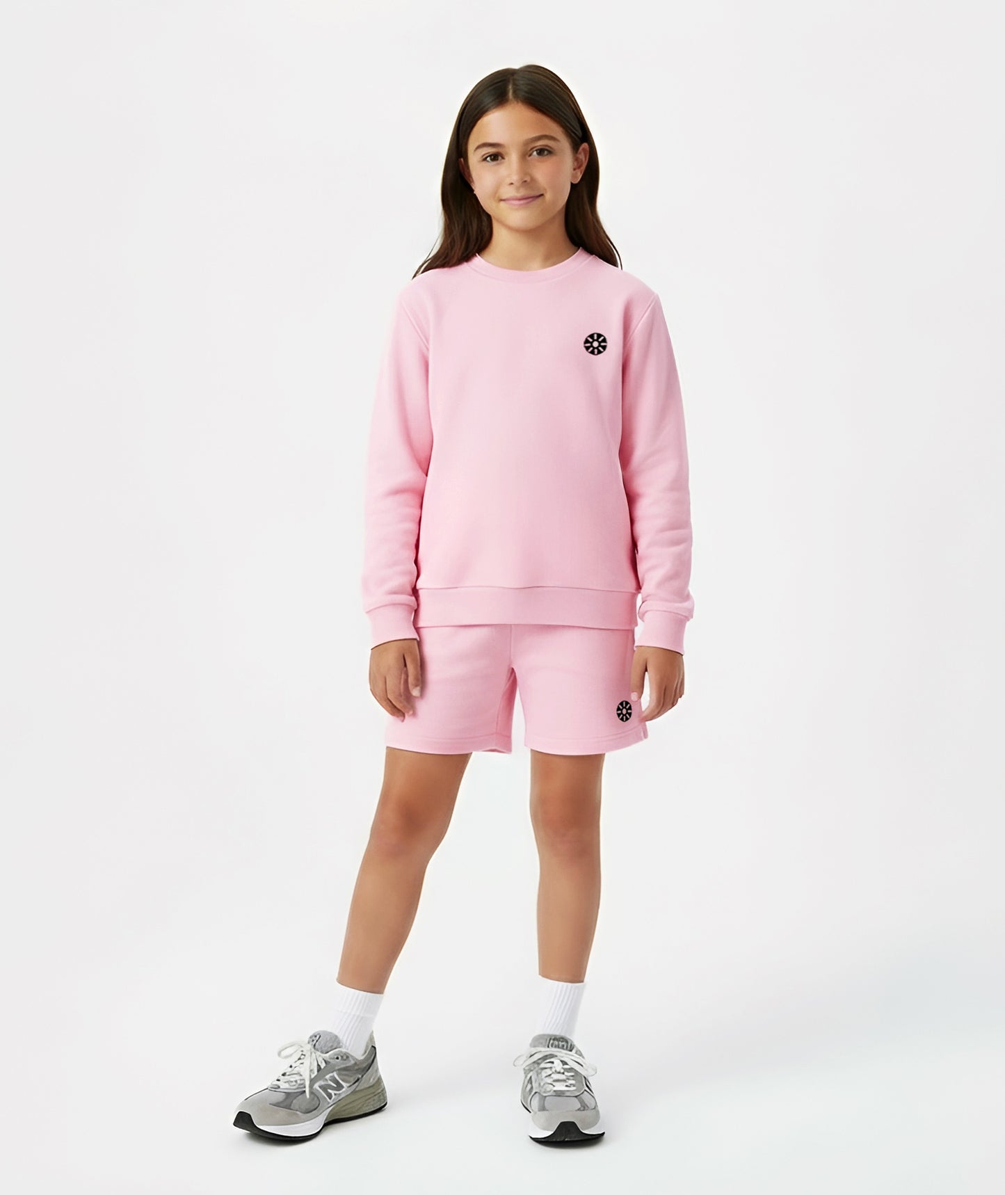 Girl wearing Goldencubs pink cotton shorts with black circular logo, styled with matching pink sweatshirt and gray sneakers.