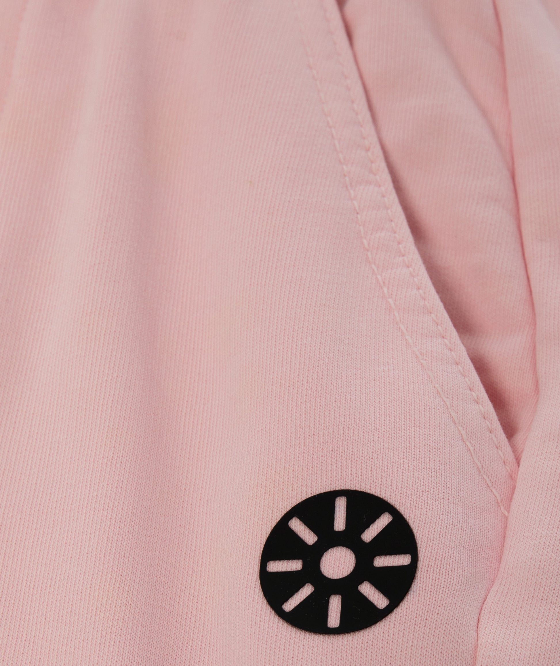 Close-up of Goldencubs black circular logo printed on soft pink cotton sweatpants fabric.