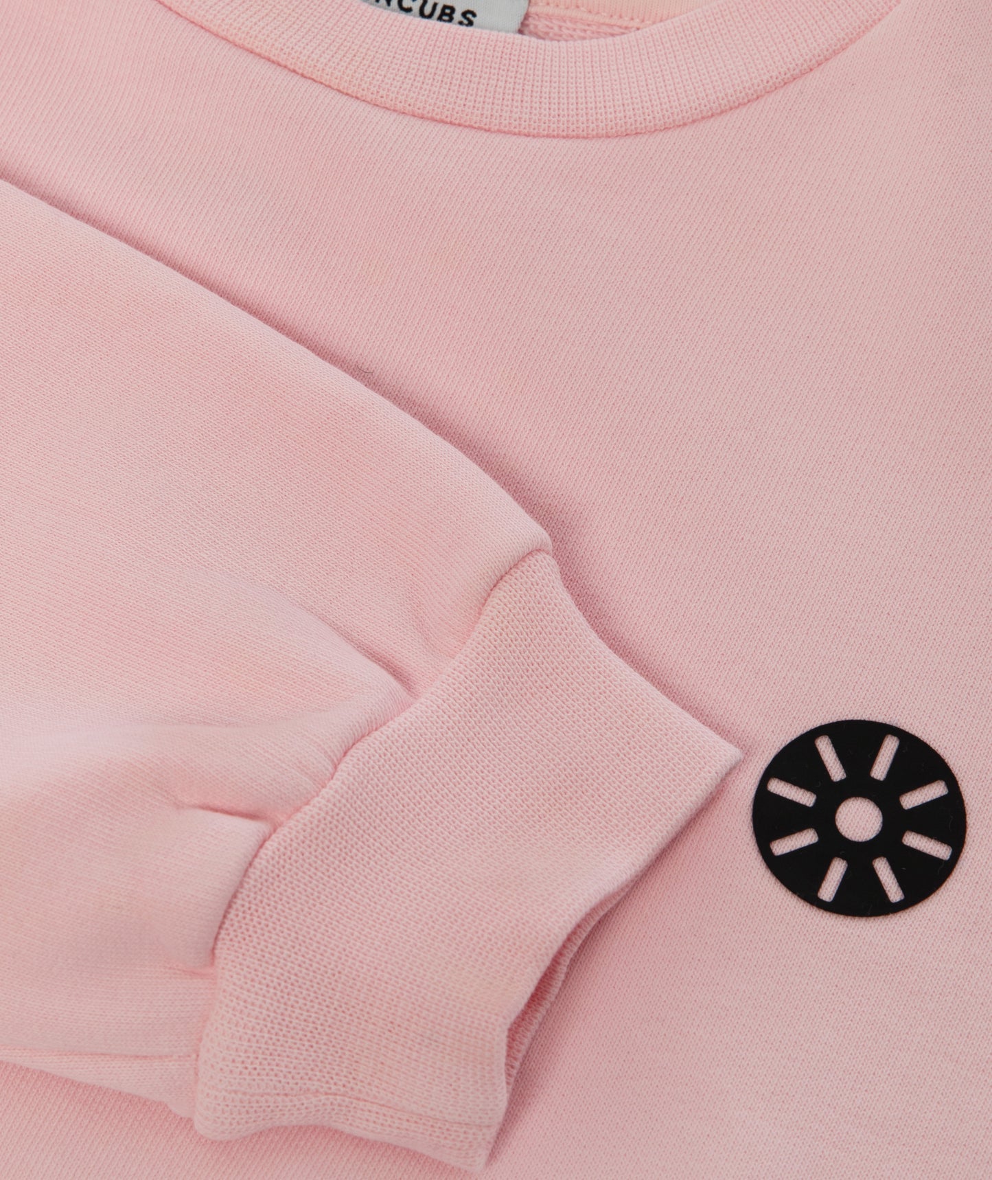 Close-up of Goldencubs black circular logo printed on soft pink cotton sweatshirt fabric.