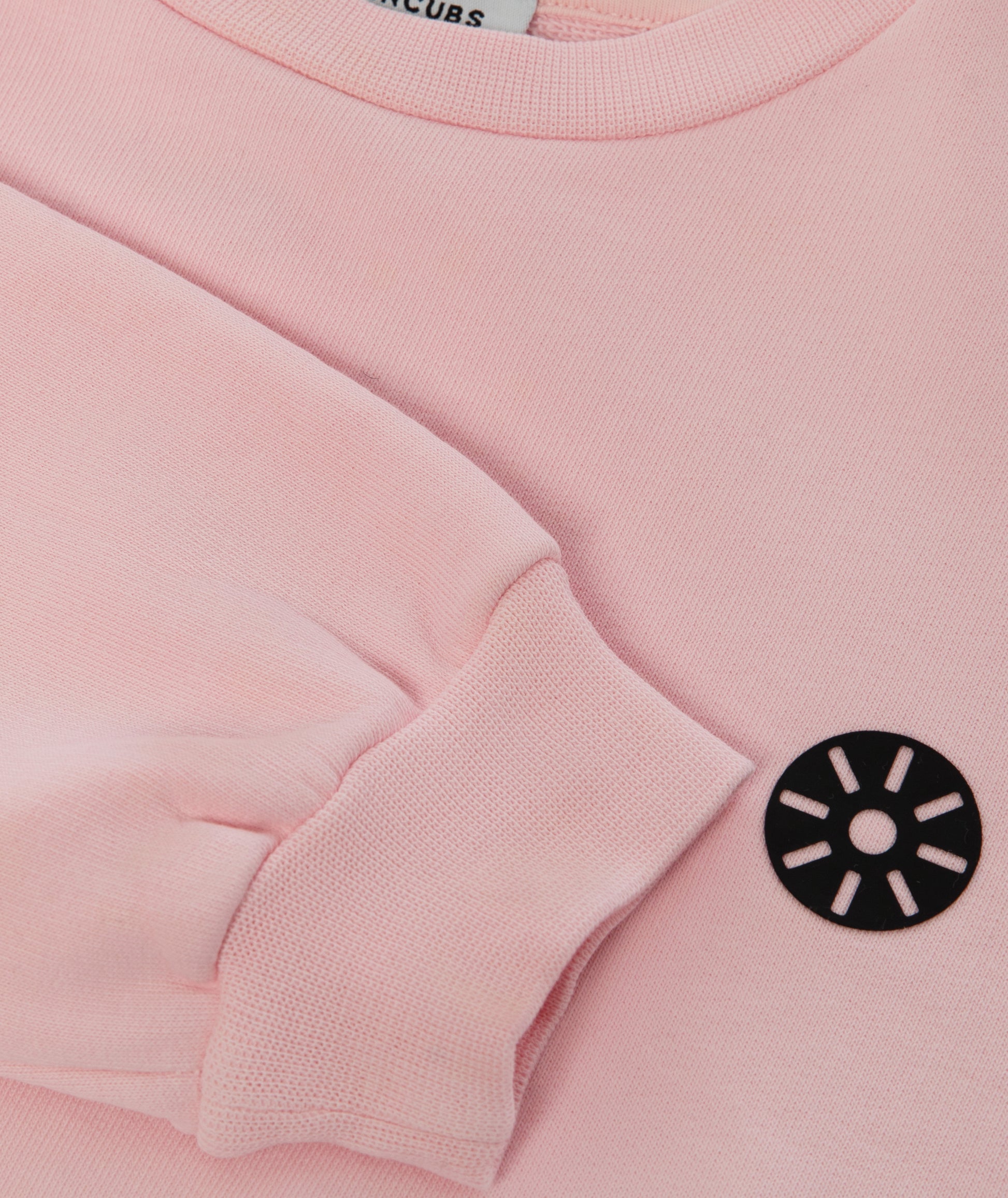 Close-up of Goldencubs black circular logo printed on soft pink cotton sweatshirt fabric.