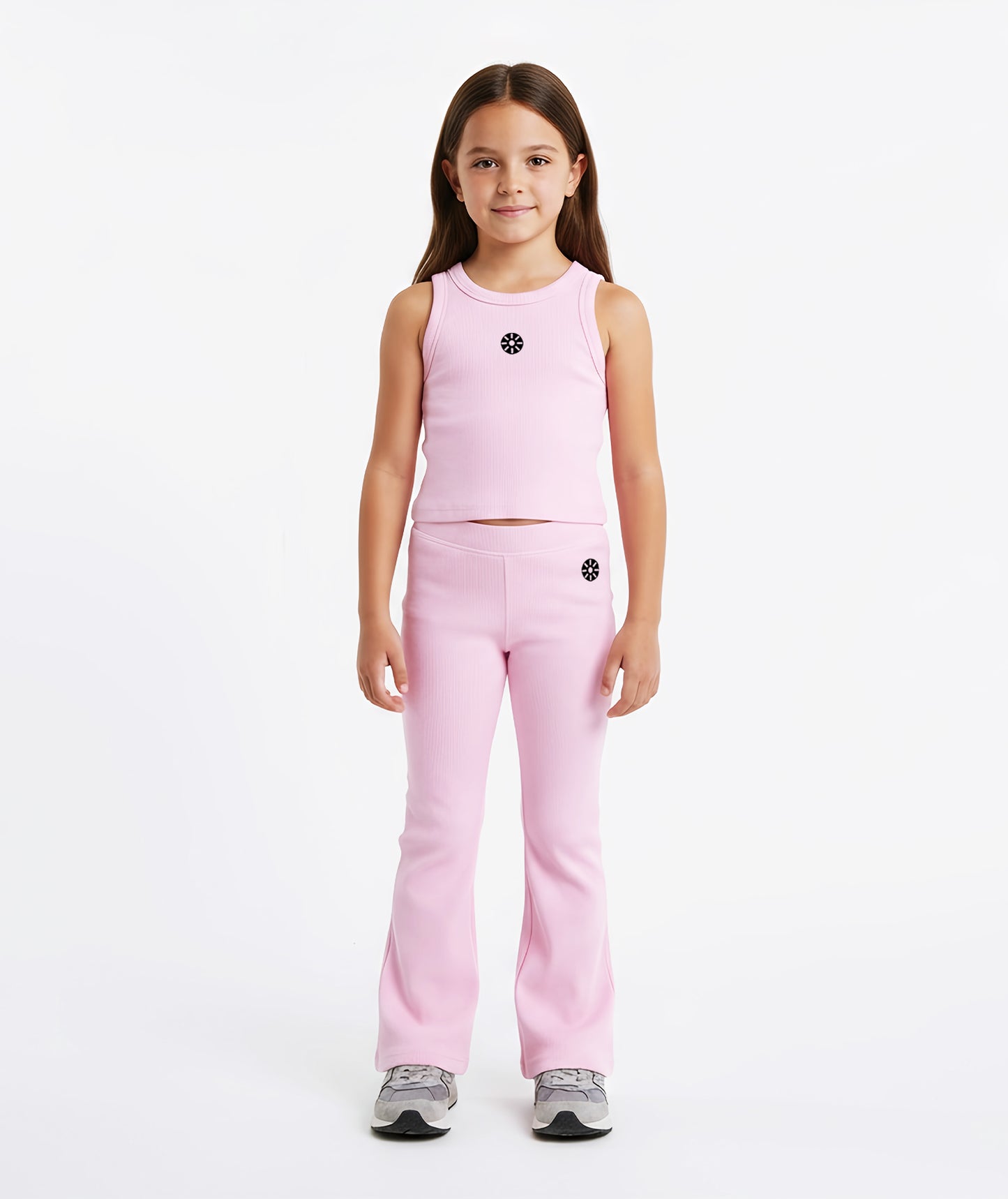 Girl wearing Goldencubs pink cotton tank top with black circular logo, paired with matching flared pants and gray sneakers.