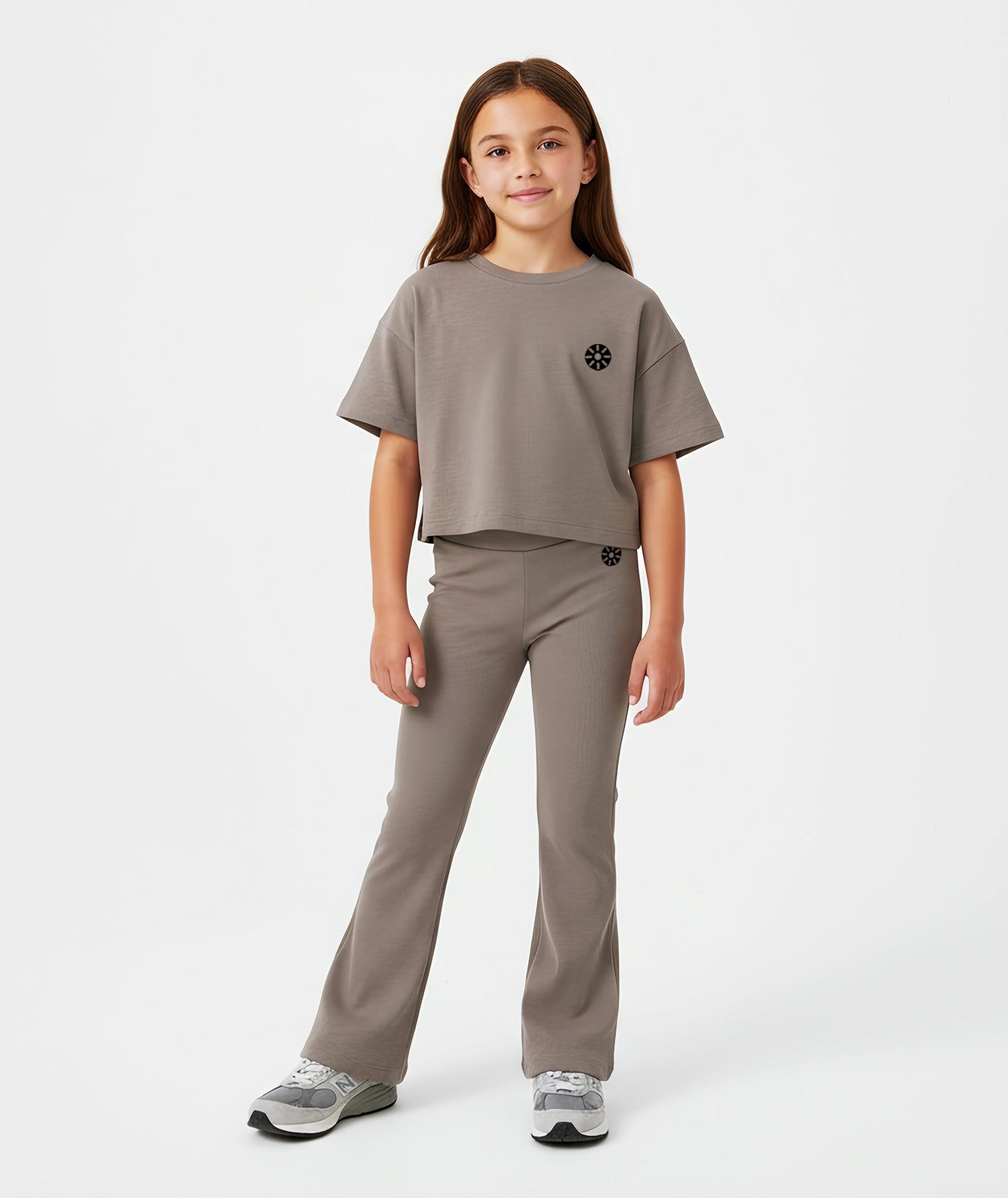 Girl wearing Goldencubs taupe cotton flared pants with black circular logo, styled with matching T-shirt and gray sneakers.
