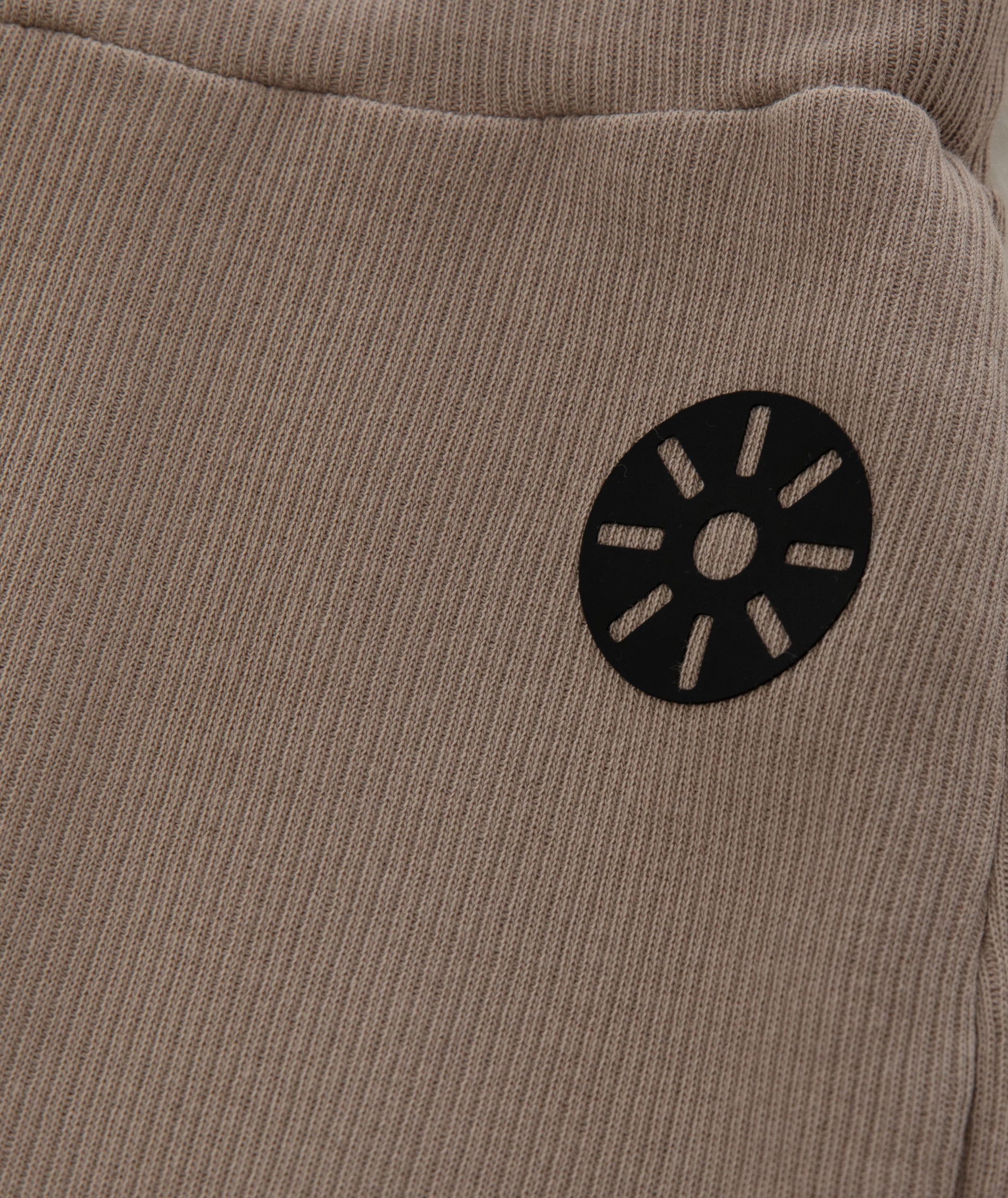 Close-up of Goldencubs black circular logo printed on soft ribbed taupe cotton fabric of the flared pants.