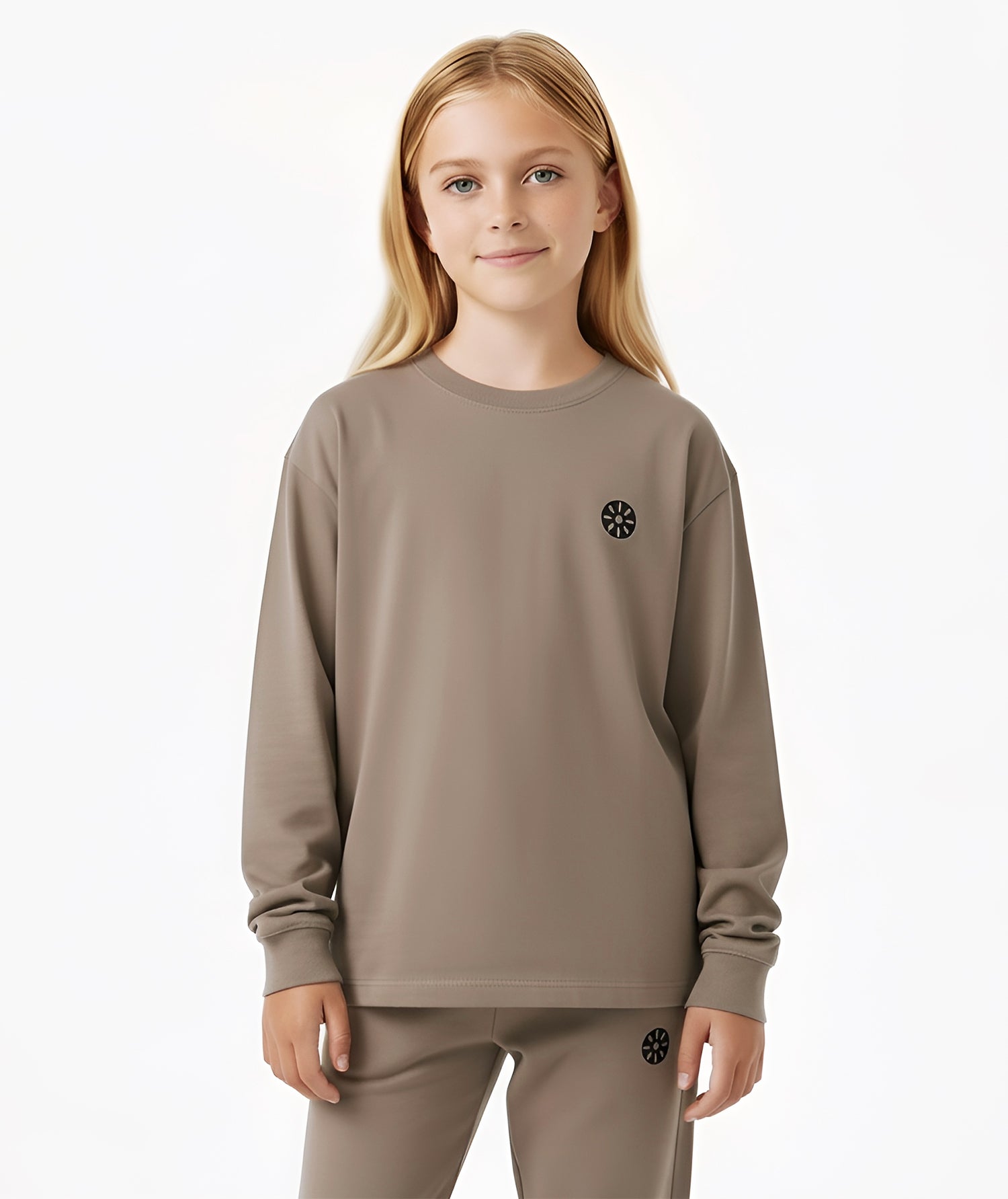 Girl in taupe Goldencubs long sleeve T-shirt with round neckline and signature black logo patch on chest.
