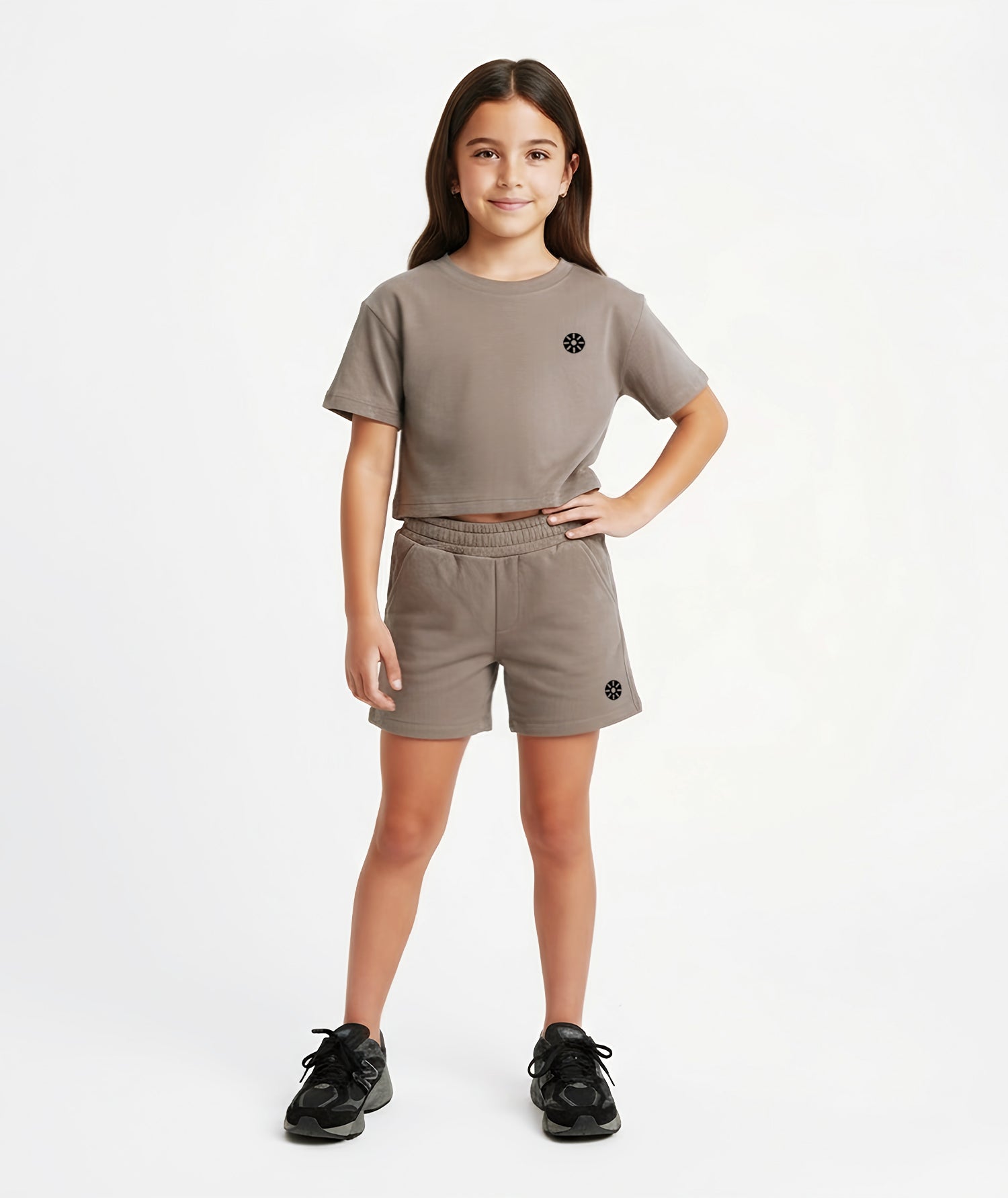 Girl wearing Goldencubs taupe cotton shorts with black circular logo, styled with matching cropped T-shirt and black sneakers.