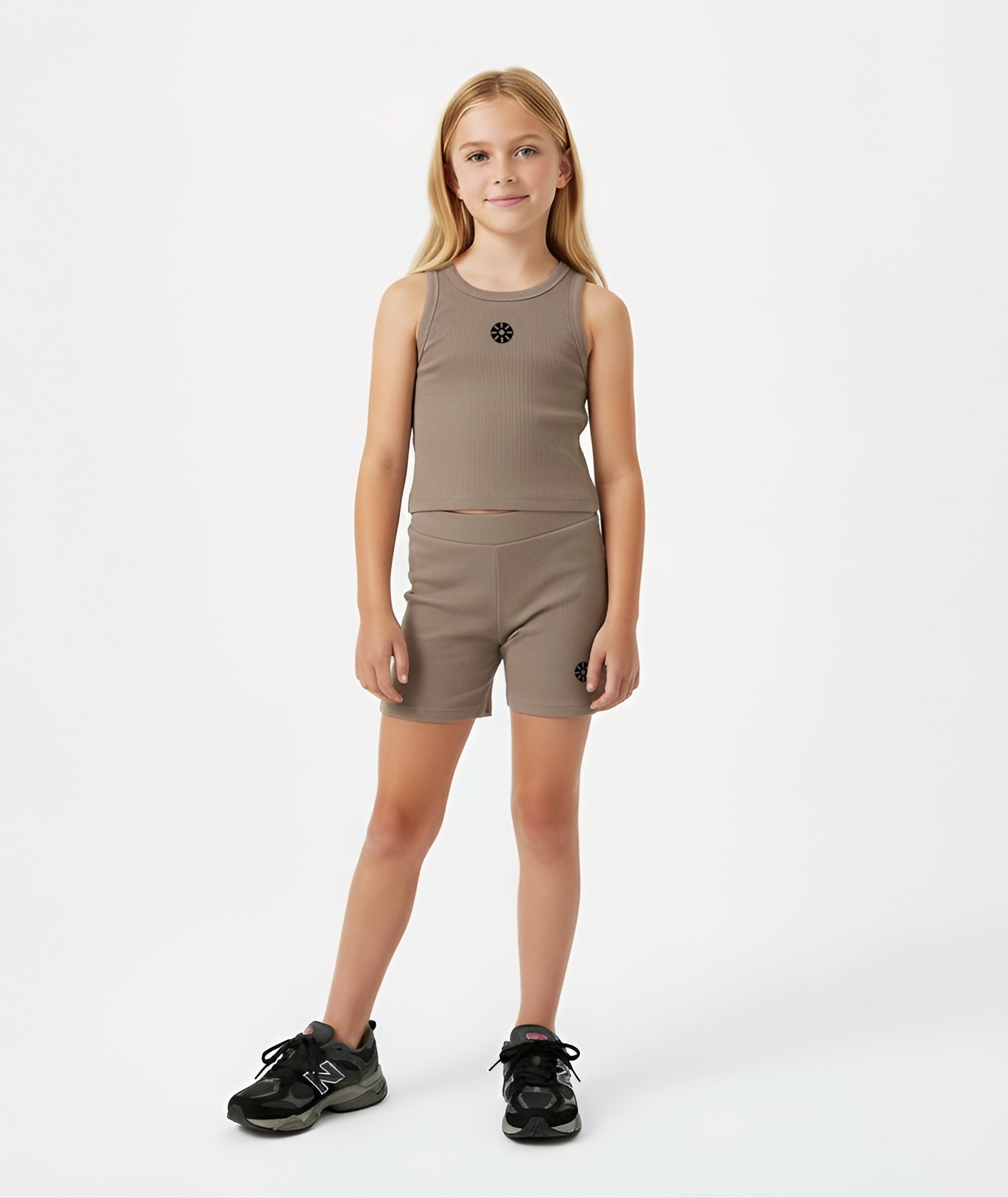 Girl wearing Goldencubs taupe cotton tank top with black circular logo, styled with matching shorts and black sneakers on a white background.