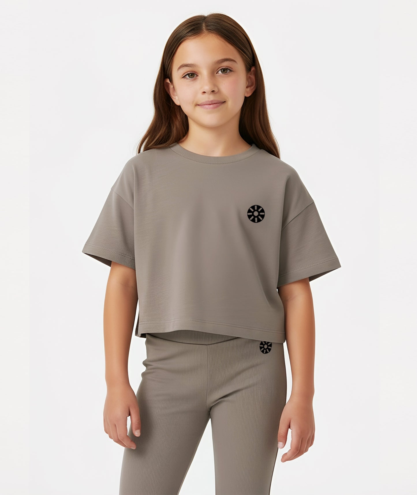 Girl wearing Goldencubs taupe cotton T-shirt with short sleeves and black circular logo, posing against a white background.