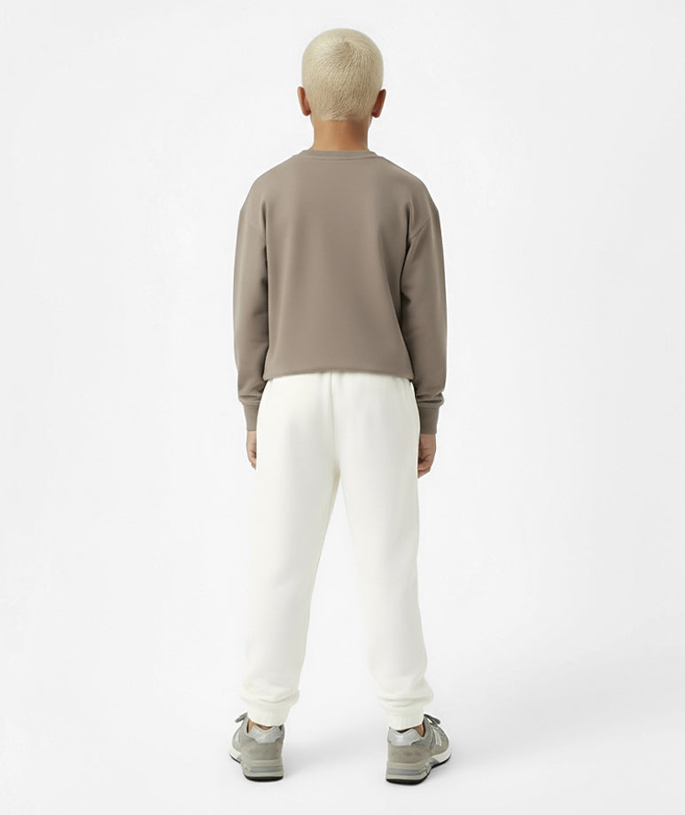 Back view of boy wearing Goldencubs taupe cotton long sleeve T-shirt paired with white sweatpants — relaxed and minimalist kids athleisure outfit.