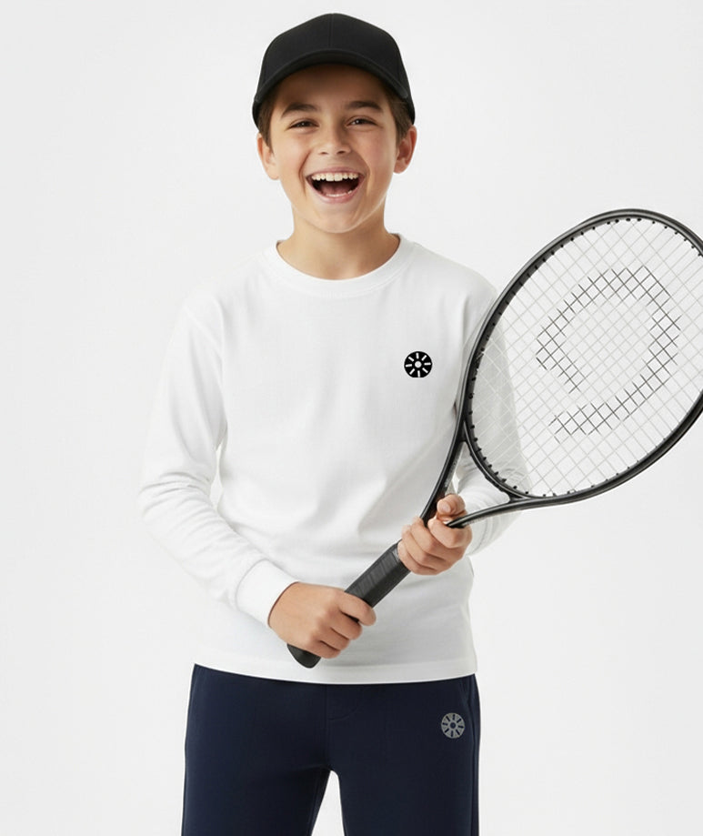 Smiling boy wearing Goldencubs white cotton long sleeve T-shirt and navy sweatpants, holding a tennis racket — comfortable and fashionable kids athleisure style.