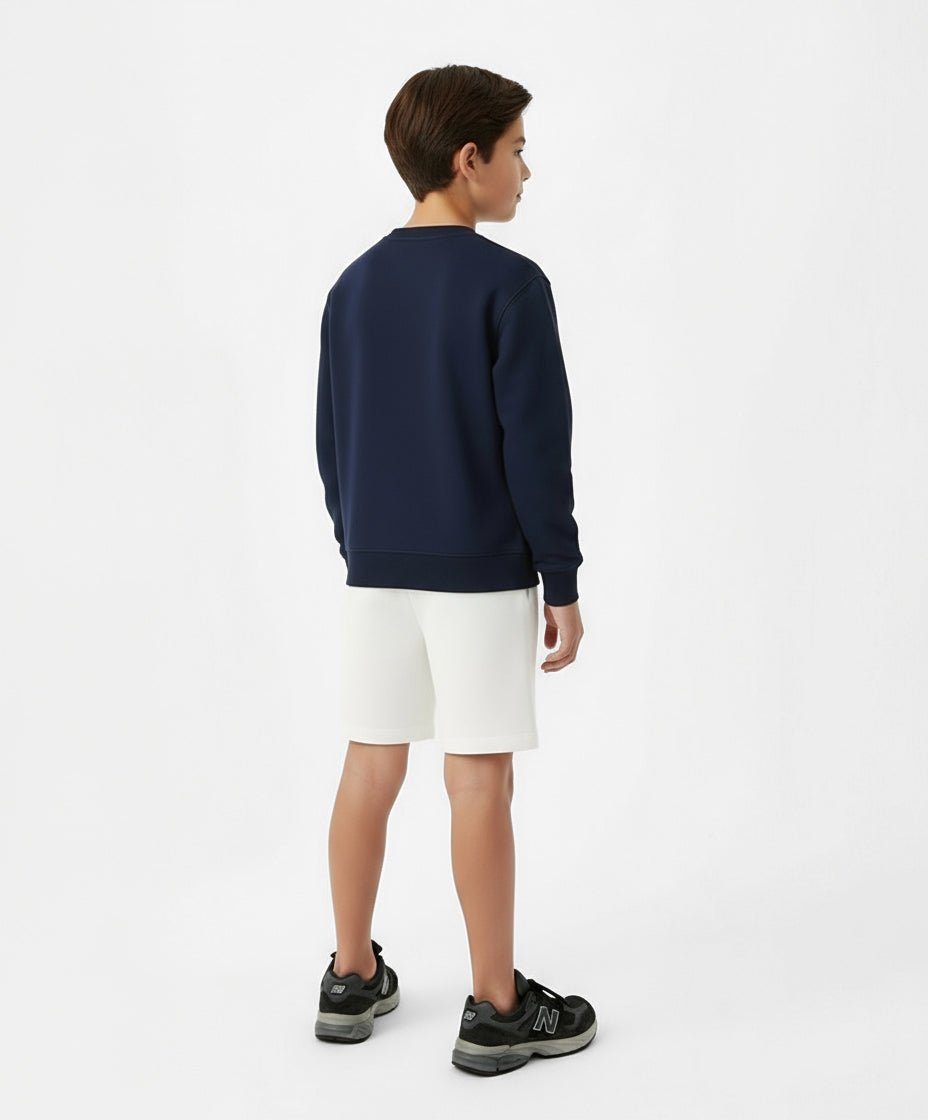 Back view of boy wearing Goldencubs white cotton boys shorts with navy sweatshirt — sporty, simple, and relaxed kids athleisure look.
