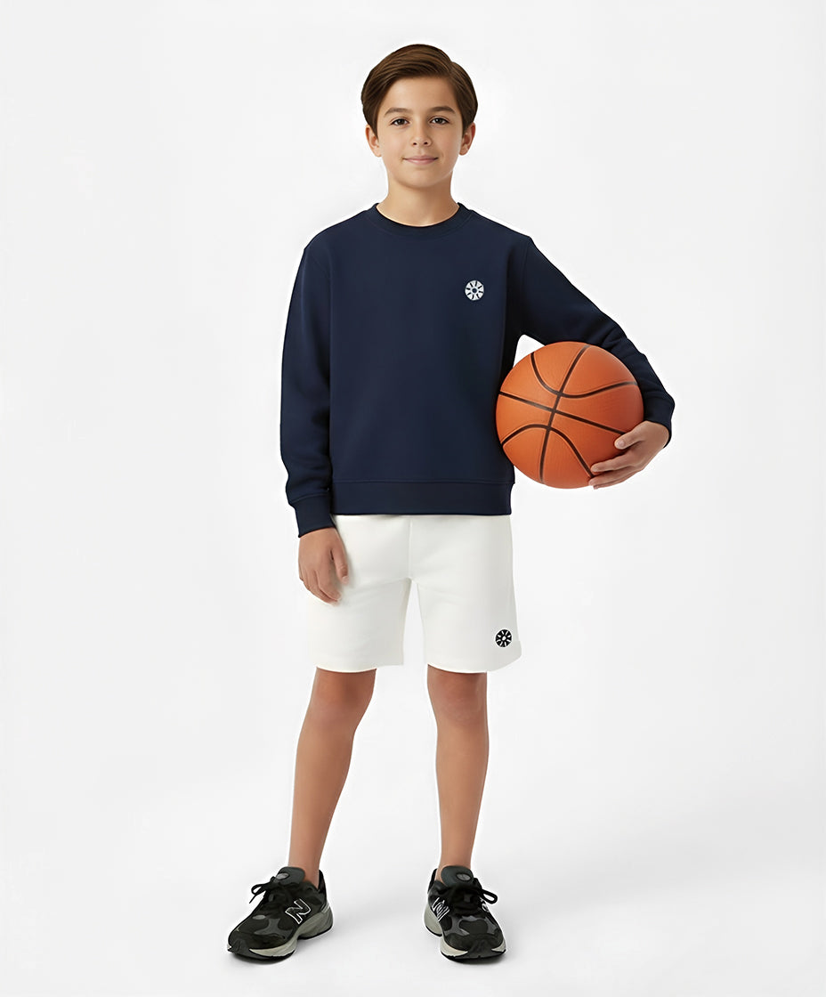 Front view of boy wearing Goldencubs white cotton boys shorts and navy sweatshirt while holding a basketball — stylish and active kidswear ensemble.