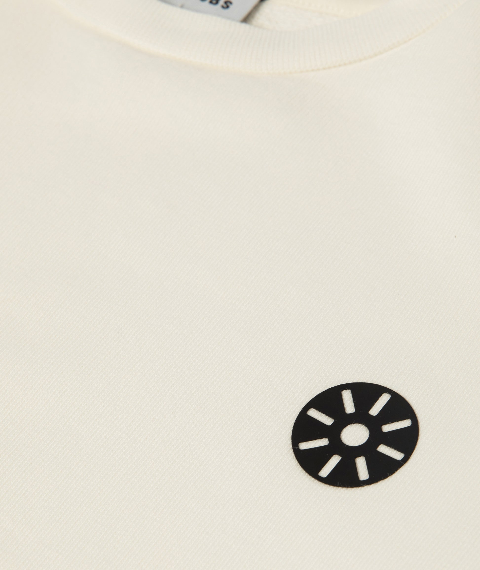 Close-up of Goldencubs white cotton girls sweatshirt featuring soft ribbed collar and black circular logo patch — premium kids athleisurewear fabric detail.