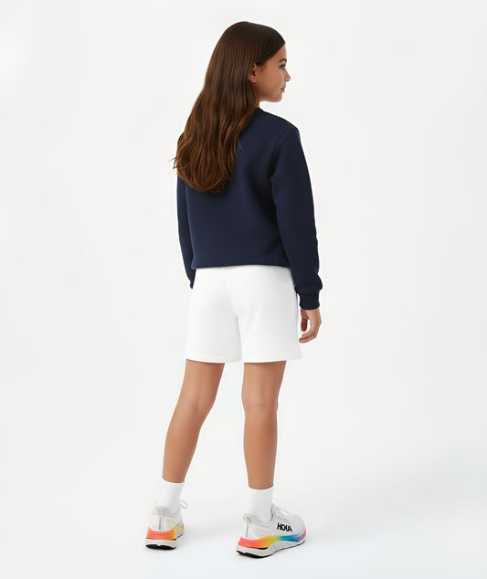 Rear view of a girl in white cotton shorts and a navy sweatshirt, showcasing the clean design, relaxed fit, and soft cotton texture of Goldencubs kidswear.