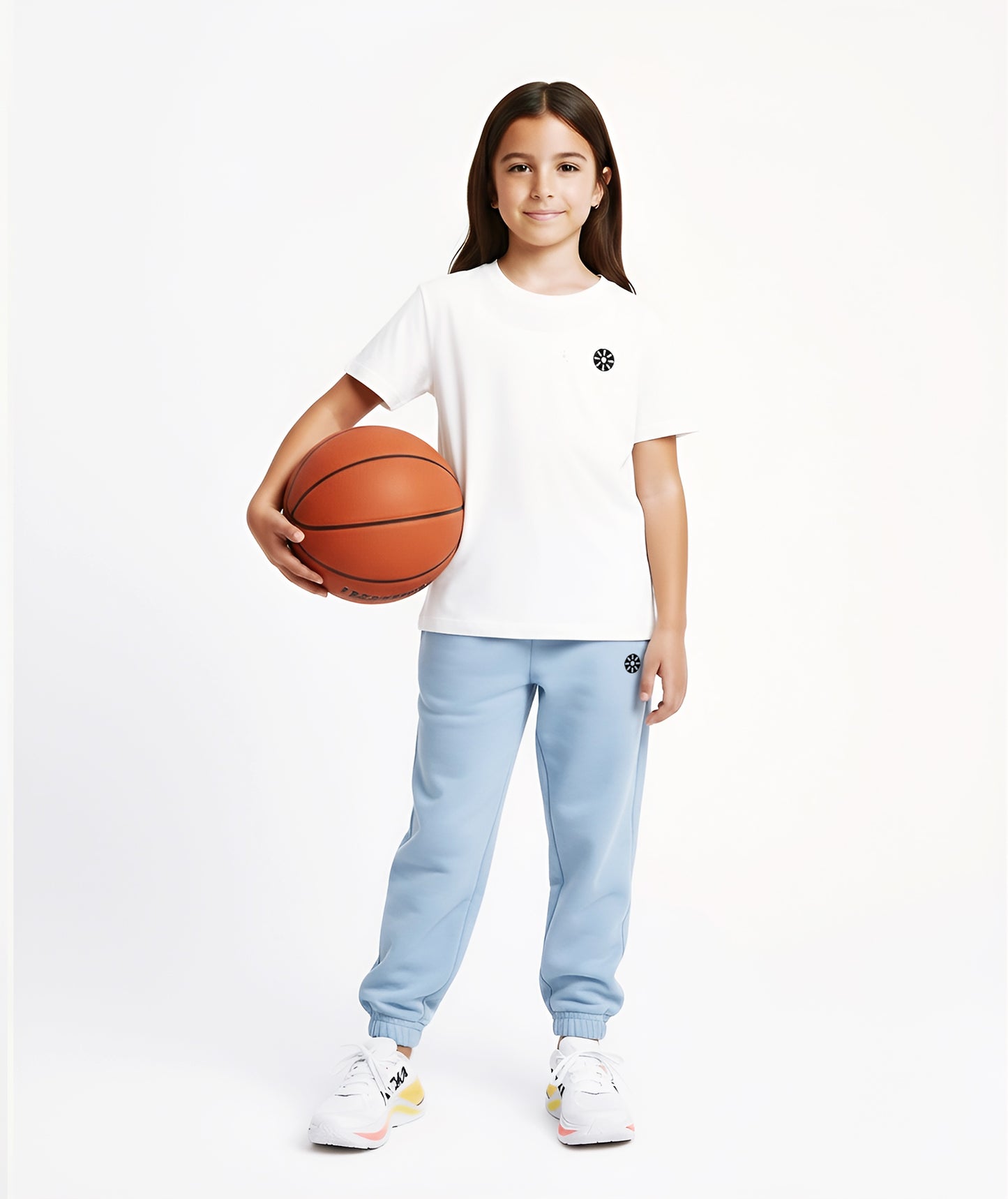 A sporty girl stands confidently holding a basketball while wearing a white cotton T-shirt with a minimal black logo and light blue sweatpants, perfect for active days and casual outings.
