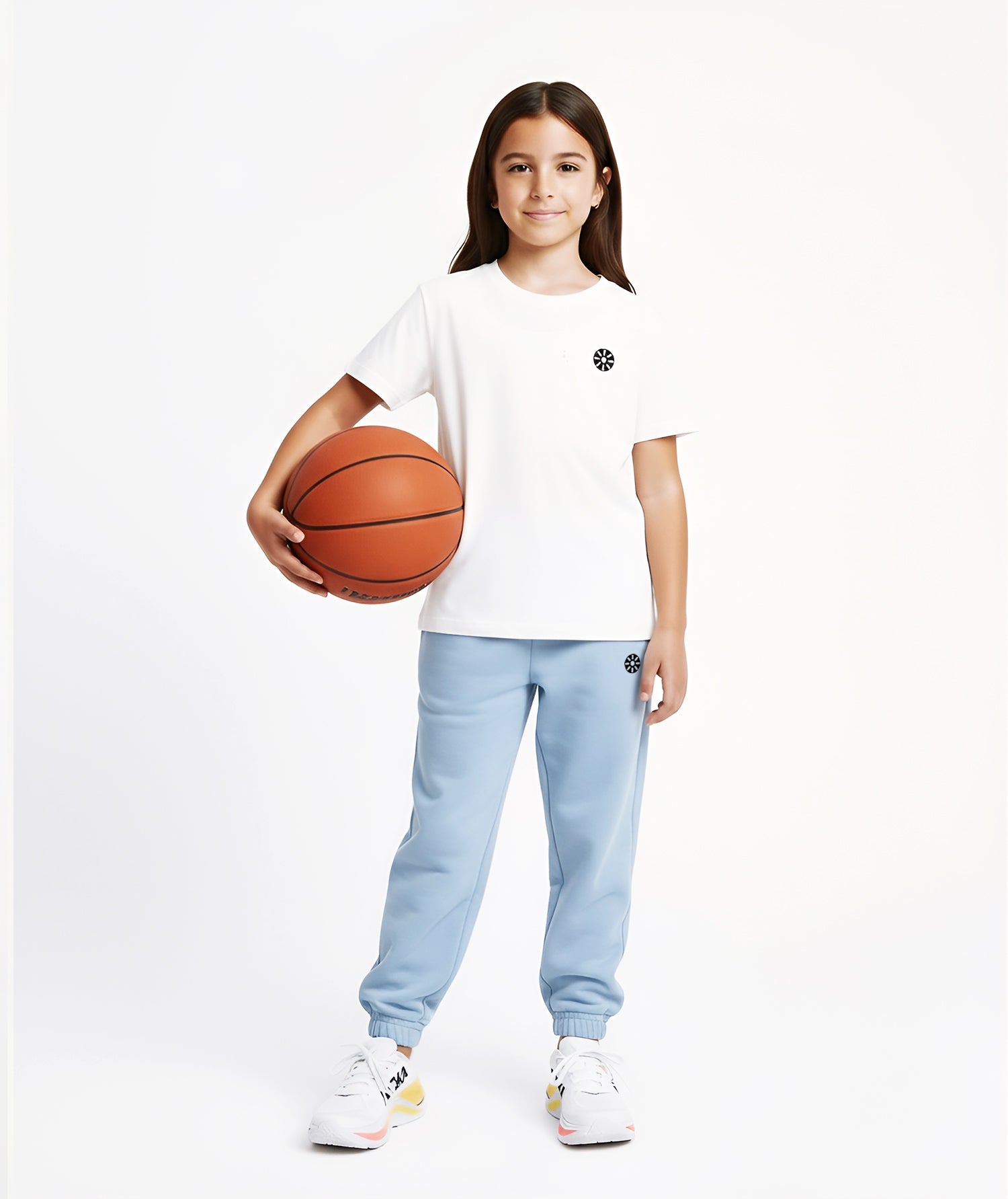 A sporty girl stands confidently holding a basketball while wearing a white cotton T-shirt with a minimal black logo and light blue sweatpants, perfect for active days and casual outings.